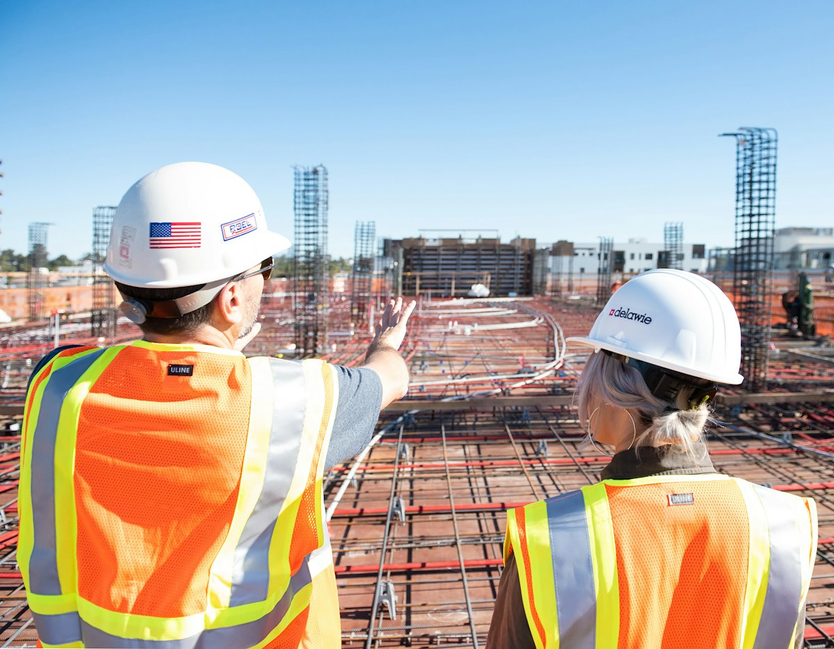 Contractor in a hard hat with a U.S. flag decal pointing out the work to a colleague